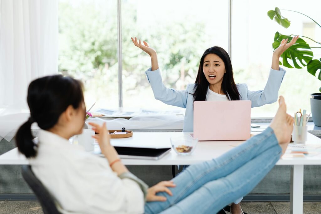 Signboard Company in Dubai Two women engage in an animated discussion in a modern office setting, surrounded by laptops and relaxed atmosphere.